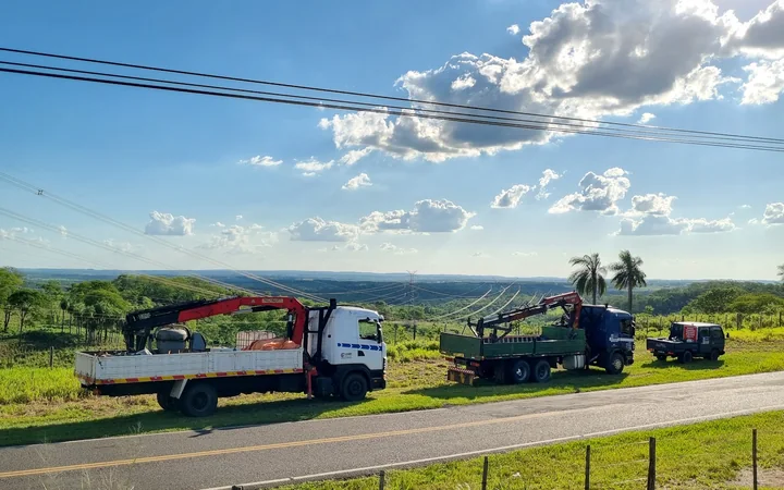 Dos camiones grúa trabajando junto a una ruta, con un valle verde de fondo