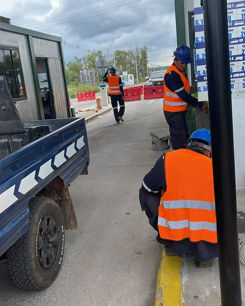 Operarios con chaleco reflectivo trabajando junto a una cabina de peaje